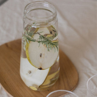 KINTO LUCE Water Carafe filled with infused water featuring pear slices and rosemary on wooden coaster