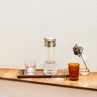 KINTO LUCE Water Carafe with stainless steel lid on wooden tray surrounded by clear and amber glasses