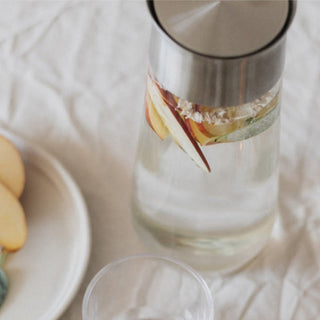 KINTO LUCE Water Carafe with stainless steel lid filled with infused water on a soft beige cloth surface