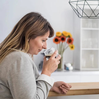 Woman enjoying coffee from KRUVE PROPEL Espresso Glasses (75ml/2.5oz) (2-Pack) in bright kitchen setting