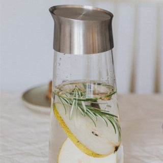 KINTO LUCE Water Carafe with stainless steel lid containing infused water with pear slices and rosemary sprig