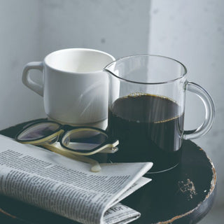 KINTO SLOW COFFEE STYLE Coffee Jug filled with black coffee next to a white cup and glasses on table